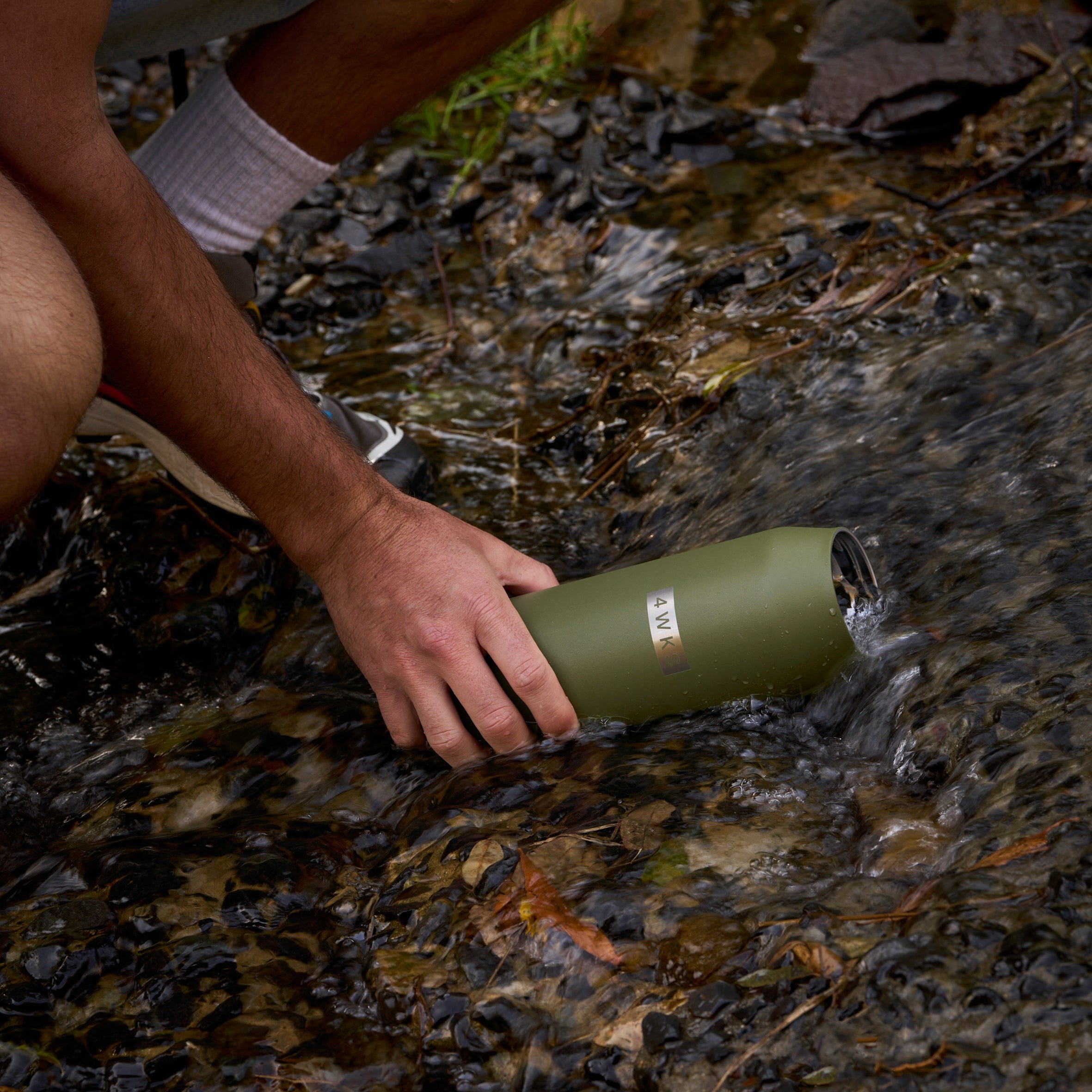 Person holding a green water bottle over a stream